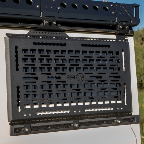 A Black Exterior cargo carrier made by Rough Road Equipment with the RRE logo stamped into it, shown on an Ineos Grenadier. Featuring three different attachment points for various systems like L-track (Airline Track), MOLLE, and Carrage bolt. Show with the optional LeTech roof rack attachment mount and the LeTech roof rack.