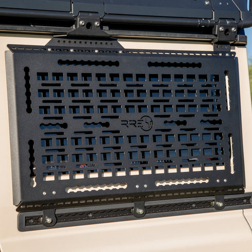 A Black Exterior cargo carrier made by Rough Road Equipment with the RRE logo stamped into it, shown on an Ineos Grenadier. Featuring three different attachment points for various systems like L-track (Airline Track), MOLLE, and Carrage bolt. Show with the optional LeTech roof rack attachment mount and the LeTech roof rack.