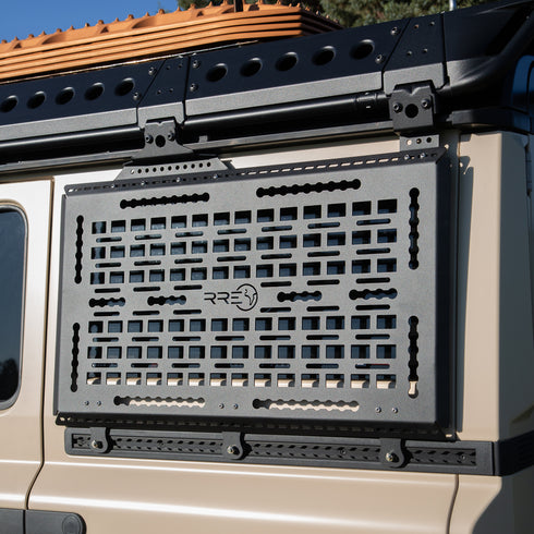 A Black Exterior cargo carrier made by Rough Road Equipment with the RRE logo stamped into it, shown on an Ineos Grenadier. Featuring three different attachment points for various systems like L-track (Airline Track), MOLLE, and Carrage bolt. Show with the optional LeTech roof rack attachment mount and the LeTech roof rack. MaxTraxx not included.
