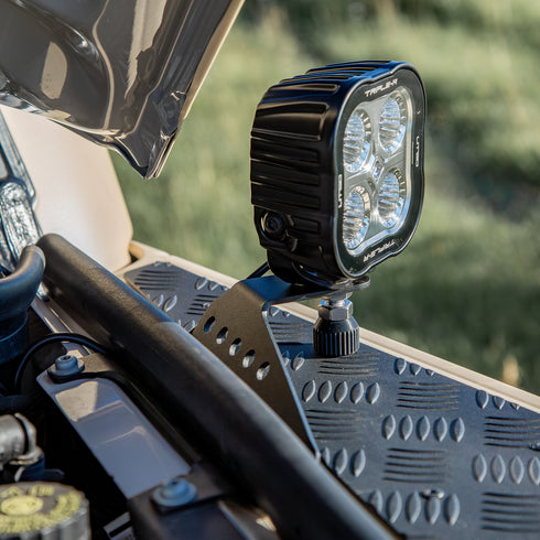 A powder-coated black aluminum Ditch Light Bracket and LED Triple-R Brand Offroad LED light mounted on the edge of the hood with no drilling needed, showing a Spacer to reduce vibration and bouncing of the light mounted on the Ineos Grenadier or Quartermaster. This image Shows how the Bracket attaches to Factory screw mounts and goes under the existing Bulb seal