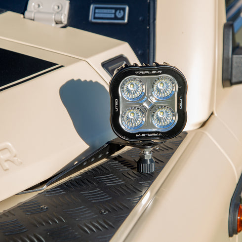 A powder-coated black aluminum Ditch Light Bracket and LED Triple-R Brand Off-road LED light mounted on the edge of the hood with no drilling needed, showing a Spacer to reduce vibration and bouncing of the light.
LED ditch light attached to a vehicle's hood.