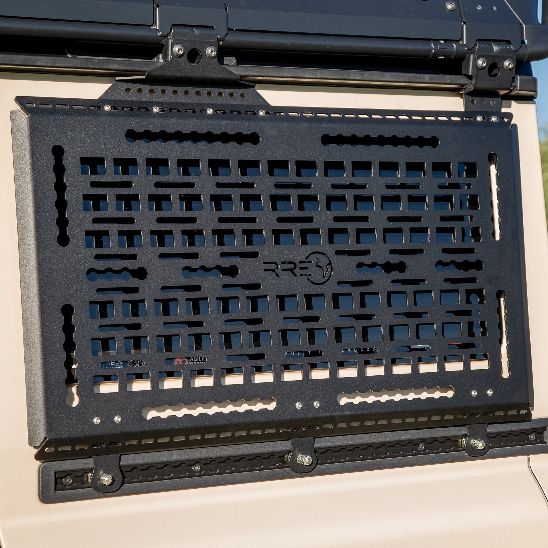 A Black Exterior cargo carrier made by Rough Road Equipment with the RRE logo stamped into it, shown on an Ineos Grenadier. Featuring three different attachment points for various systems like L-track (Airline Track), MOLLE, and Carrage bolt. Show with the optional LeTech roof rack attachment mount and the LeTech roof rack. 