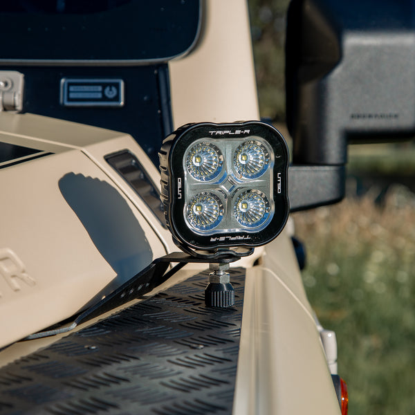A powder-coated black aluminum Ditch Light Bracket and LED Triple-R Brand Offroad LED light mounted on the edge of the hood with no drilling needed, showing a Spacer to reduce vibration and bouncing of the light mounted on the Ineos Grenadier or Quartermaster. 
Off-road vehicle with a large LED light attached to the back