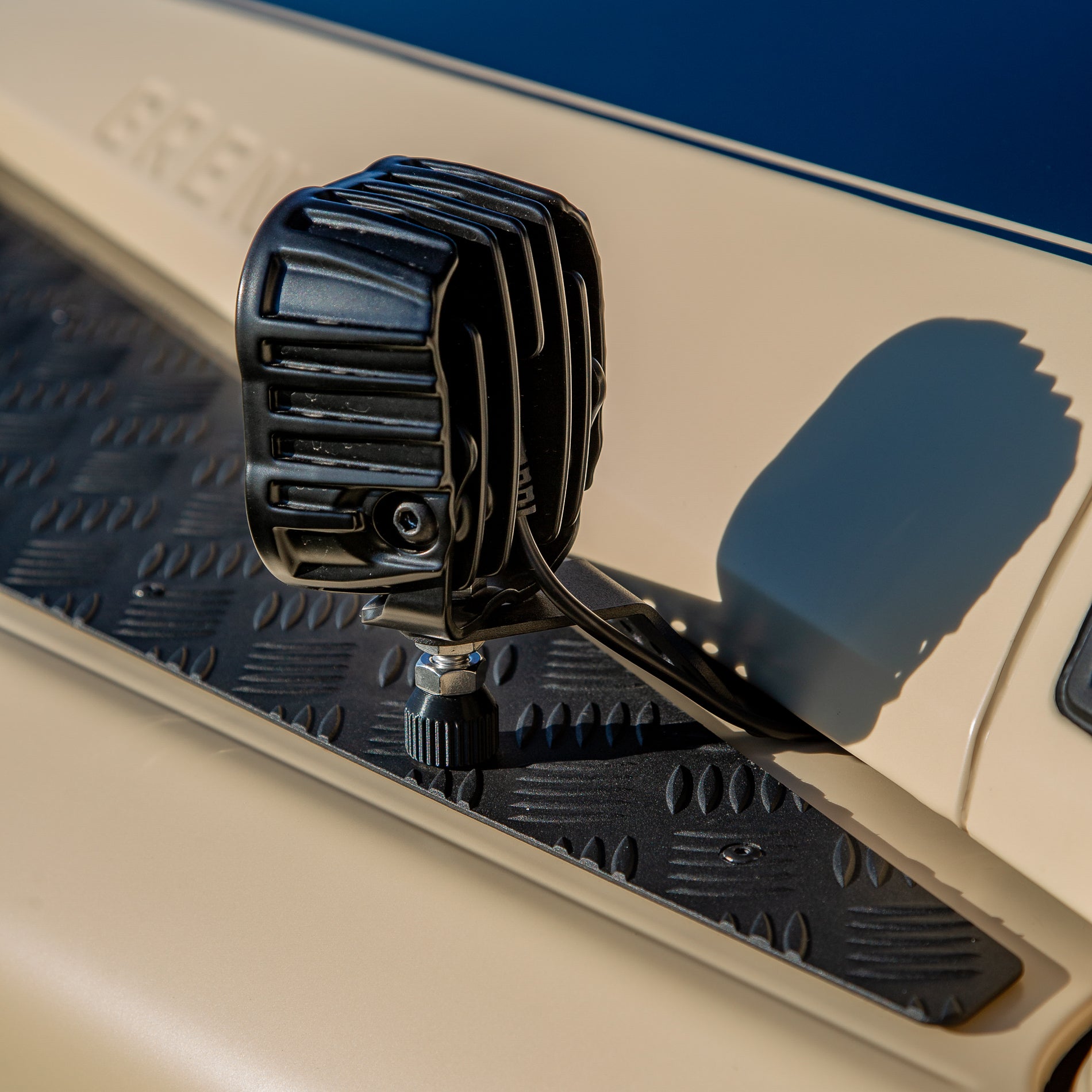 A powder-coated black aluminum Ditch Light Bracket and LED Triple-R Brand Offroad LED light mounted on the edge of the hood with no drilling needed, showing a Spacer to reduce vibration and bouncing of the light mounted on the Ineos Grenadier or Quartermaster. 
Black off-road light mounted on a vehicle