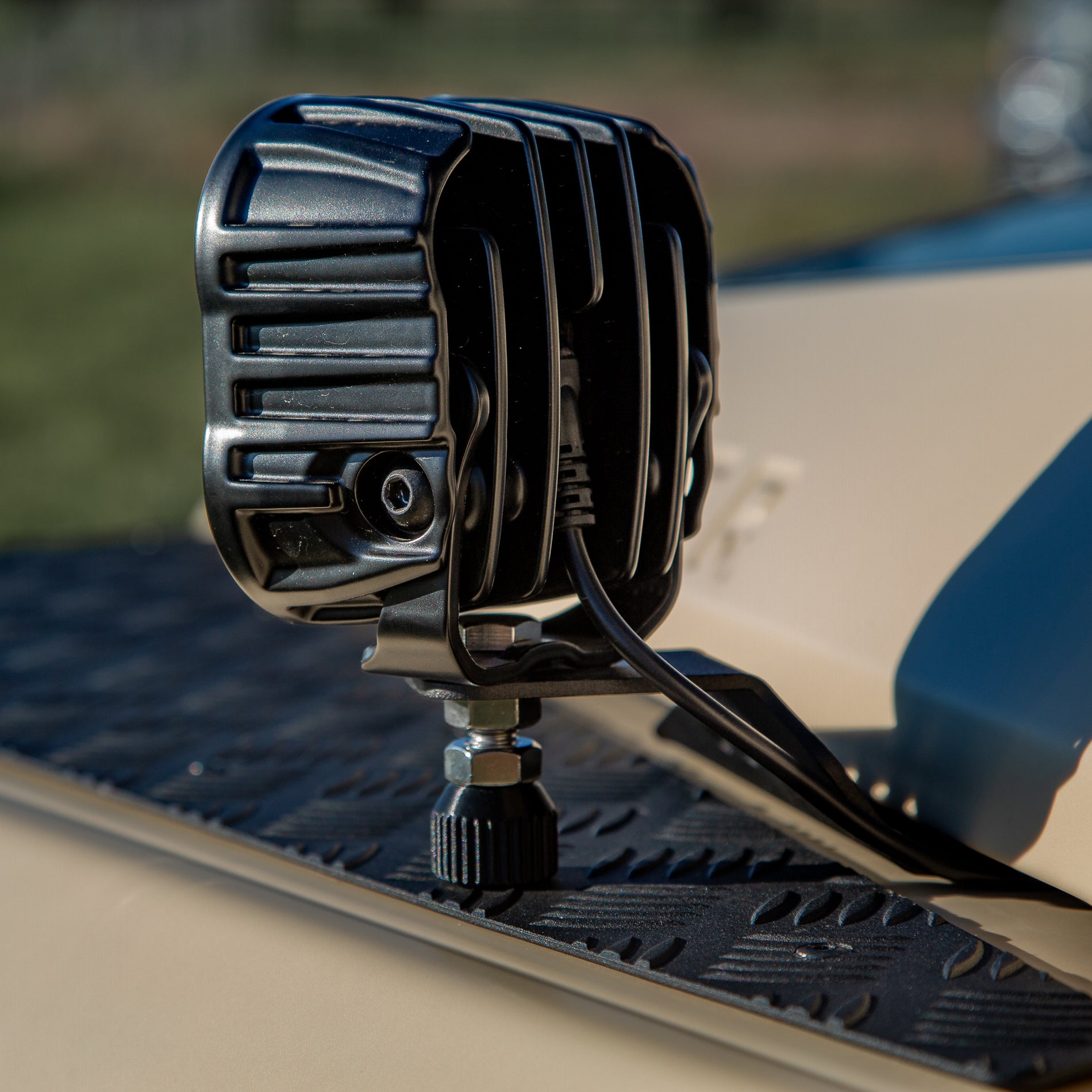 A powder-coated black aluminum Ditch Light Bracket and LED Triple-R Brand Offroad LED light mounted on the edge of the hood with no drilling needed, showing a Spacer to reduce vibration and bouncing of the light mounted on the Ineos Grenadier or Quartermaster. 
Black off-road light mounted on a vehicle