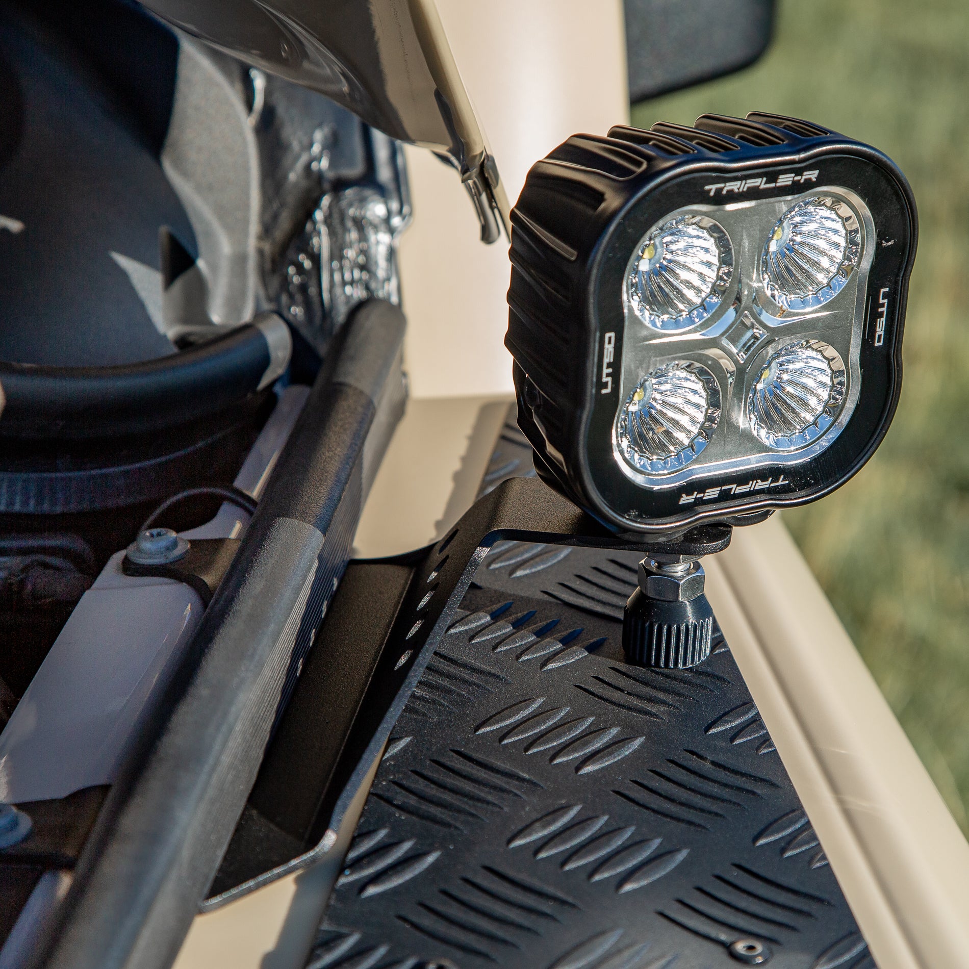 A powder-coated black aluminum Ditch Light Bracket and LED Triple-R Brand Offroad LED light mounted on the edge of the hood with no drilling needed, showing a Spacer to reduce vibration and bouncing of the light mounted on the Ineos Grenadier or Quartermaster. 

