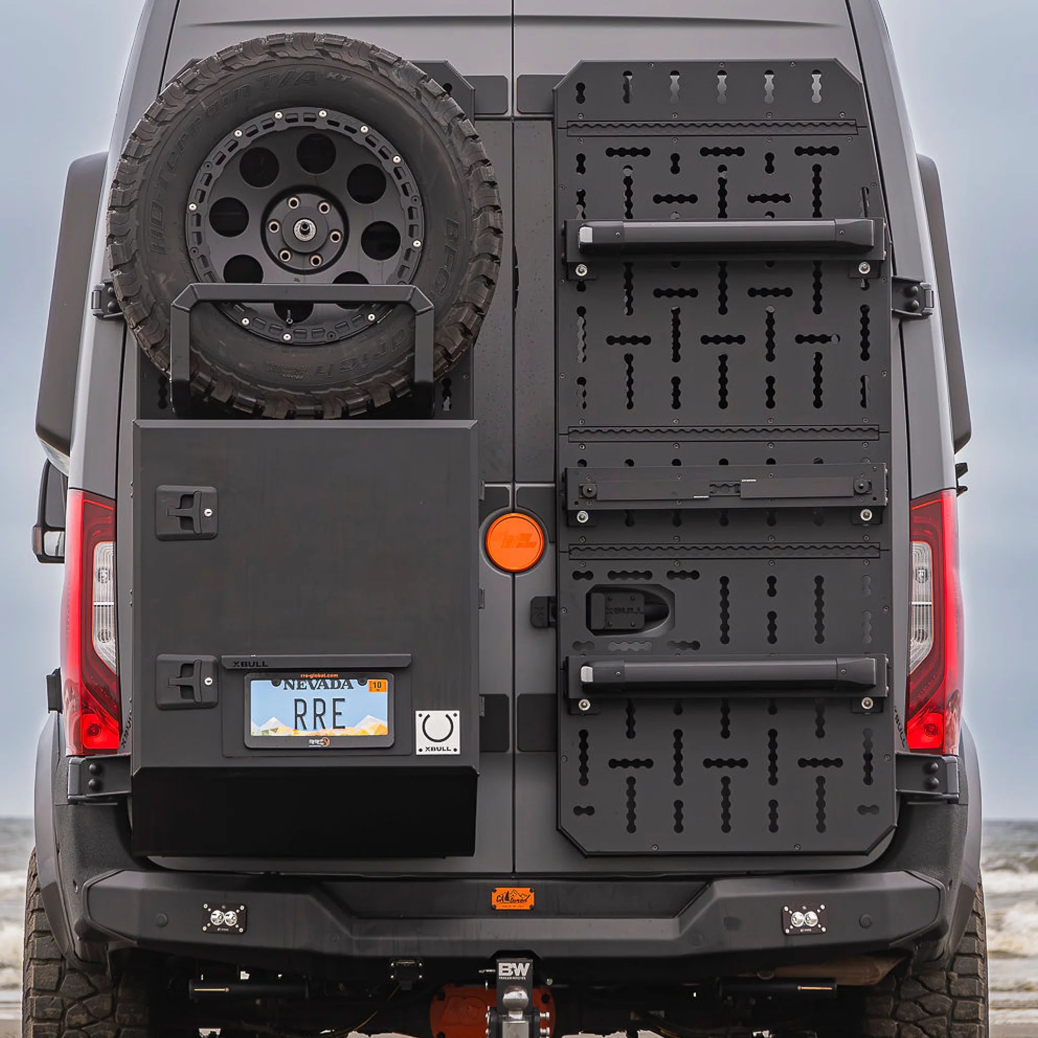 X-Bull aluminum cargo carrier mounted to a Sprinter rear door, holding a full-size spare tire and gear box.