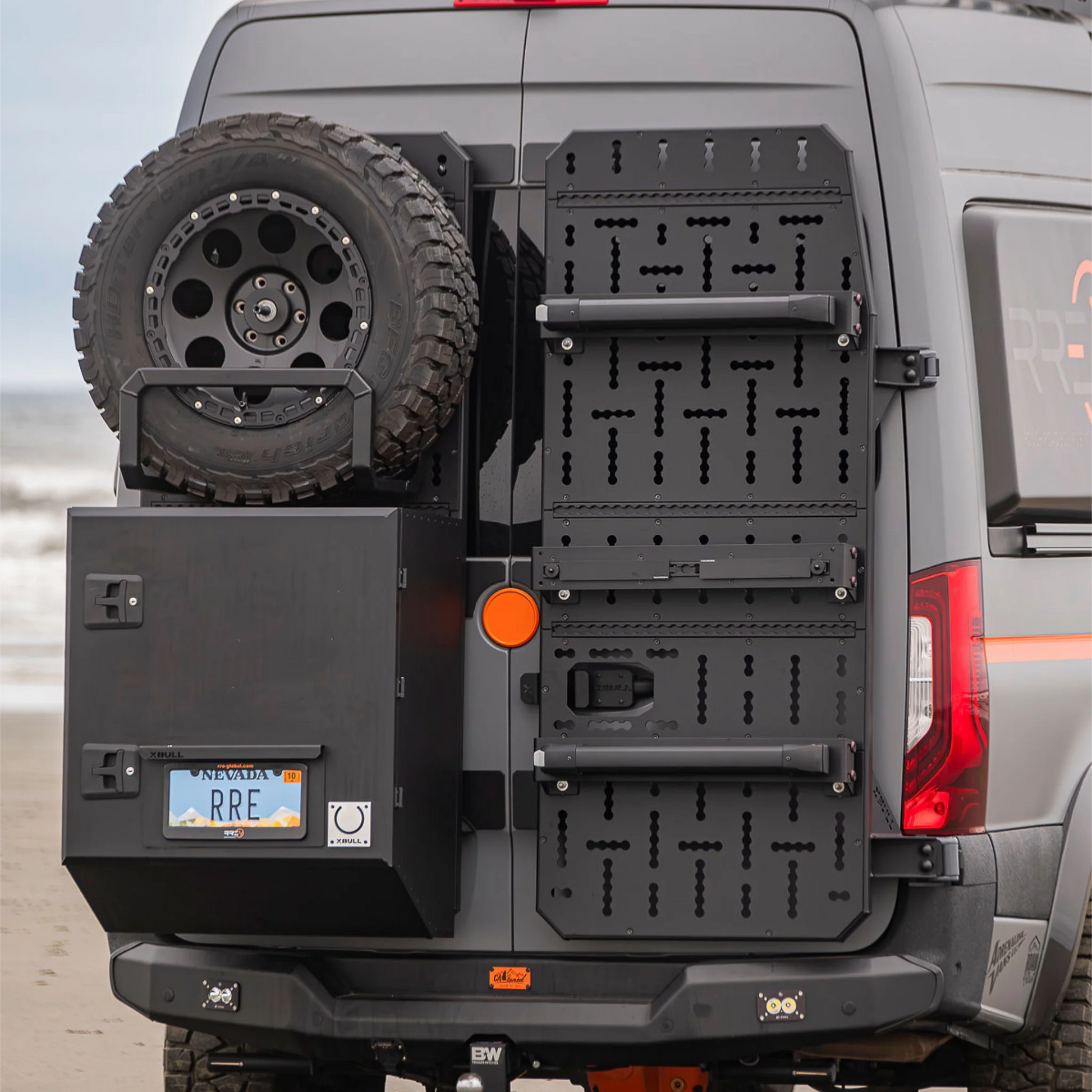 X-Bull aluminum cargo carrier mounted to a Sprinter rear door, holding a full-size spare tire and gear box.