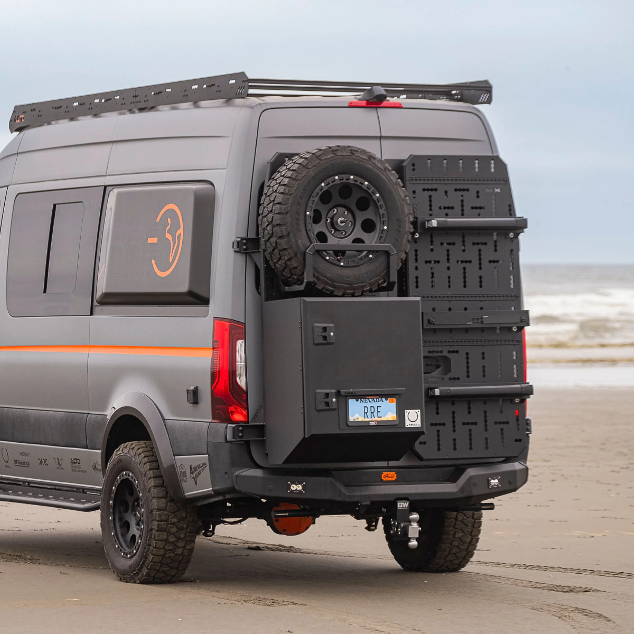 X-Bull aluminum cargo carrier mounted to a Sprinter rear door, holding a full-size spare tire and gear box.