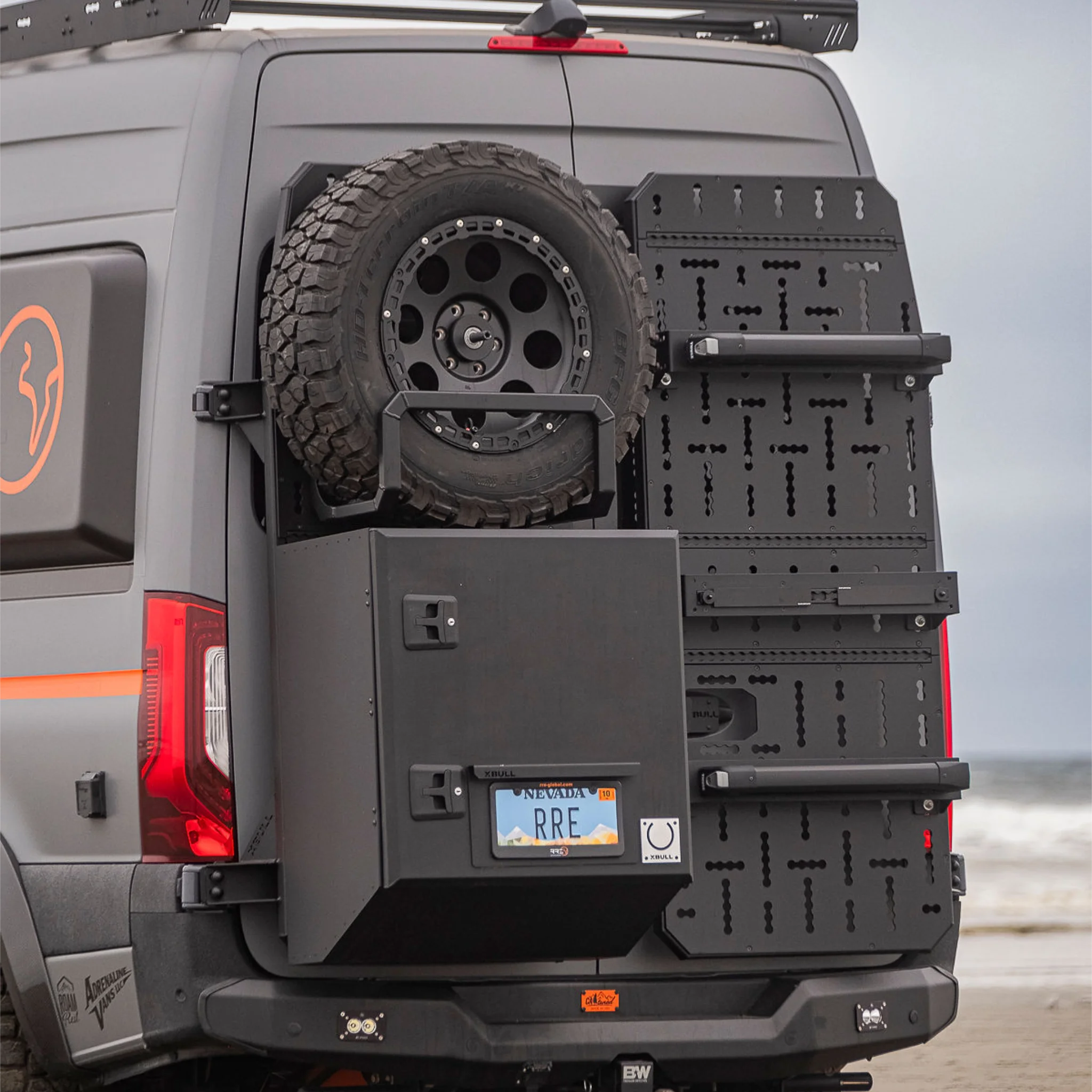 X-Bull aluminum cargo carrier mounted to a Sprinter rear door, holding a full-size spare tire and gear box.